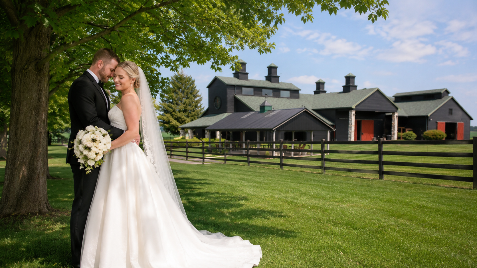 Bride and groom embracing under a tree with The Show Barn behind them