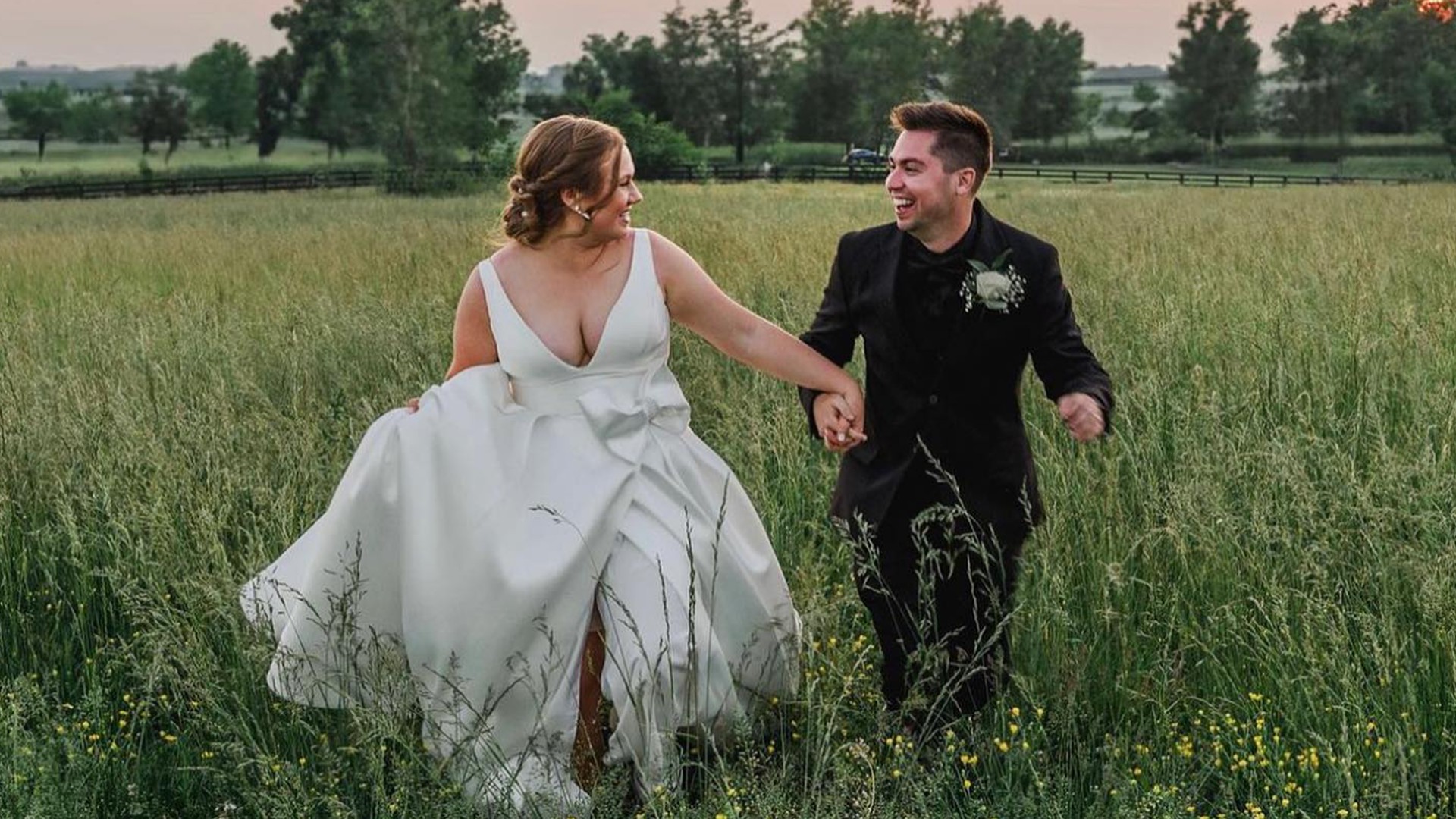 Bride and groom laughing and running through a field hand in hand